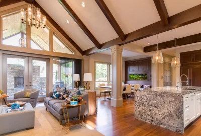 Modern open-concept living room and kitchen featuring vaulted ceilings with wood beams and a large granite island.