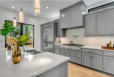 Modern kitchen with grey cabinets, white countertops, a large island, and stainless steel appliances.