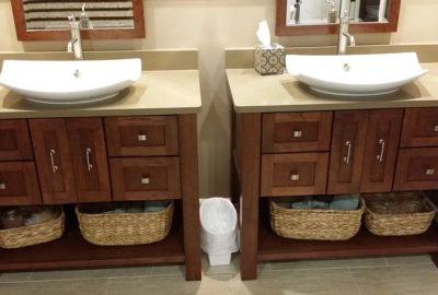 Two wooden bathroom vanities with white vessel sinks, beige countertops, and woven storage baskets underneath.