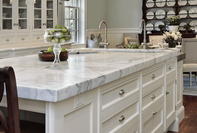 White marble kitchen island with silver faucets, a glass bowl of limes, and white cabinets.