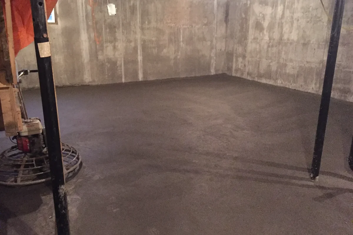 Newly poured and smoothed concrete floor in an unfinished basement with concrete walls.