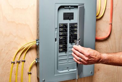 *   Image: A person's hand is reaching into an open electrical breaker panel.
    *   Context: Electrical work, home maintena