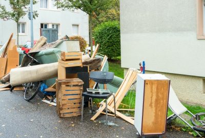 Pile of discarded furniture and household waste, including sofas and bicycles, on a sidewalk next to a building.