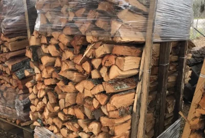 Split firewood stacked in wooden crates and partially wrapped in clear plastic.