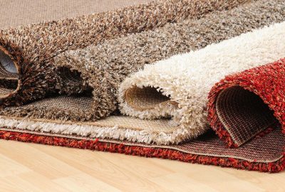 Four rolled shag rugs in brown, beige, cream, and red resting on a light wood floor.