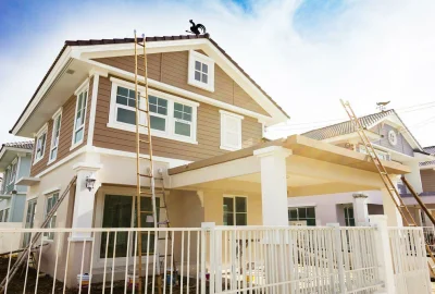 Two-story brown and beige house with white trim and bamboo ladders leaning against its exterior.