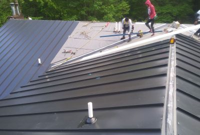 Workers installing black standing seam metal roofing panels.