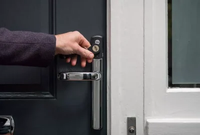 A hand using a Yale keyless entry fob to unlock a smart lock on a dark blue door.
