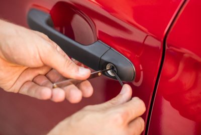 Hands using lock-picking tools to open a red car door.
