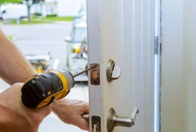 Person installing a deadbolt lock on a white door using a yellow cordless drill.