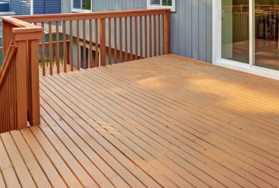 Large stained wooden deck with railings and stairs next to a house's sliding glass door.
