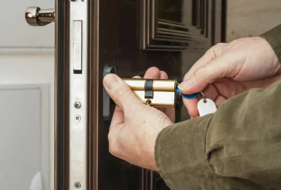 Close-up of hands installing a brass cylinder lock into a dark brown door.