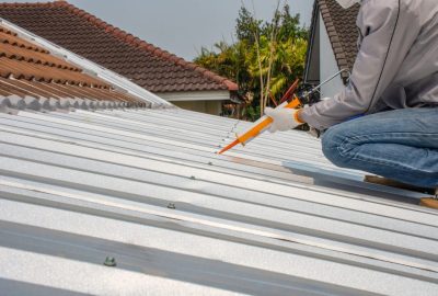 Worker applying sealant with a caulking gun to a corrugated metal roof.