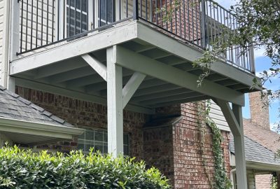 Second-story wooden deck with a black metal railing attached to a brick house with a chimney.