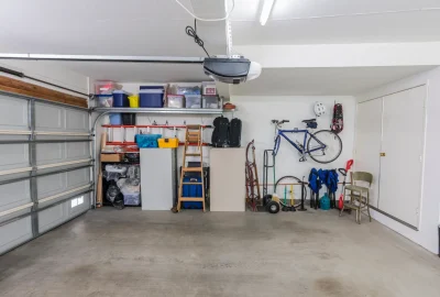 Organized garage with overhead storage bins, a wall-mounted bicycle, a wooden ladder, and various household items.