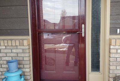 Maroon storm door beside a cream sidelight window and a blue decorative "Welcome" milk can.