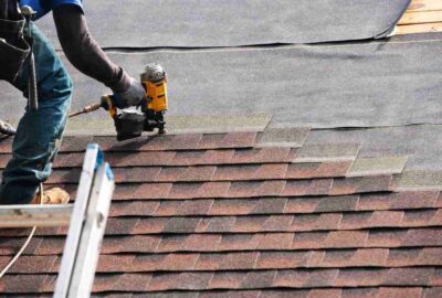 Roofer using a pneumatic nail gun to install asphalt shingles on a roof.