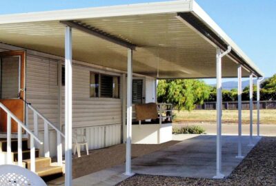 White metal carport attached to a mobile home with a concrete pad.