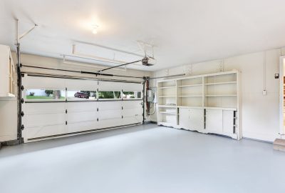 Empty garage with a white sectional door, light gray floor, and built-in white shelving units along the wall.