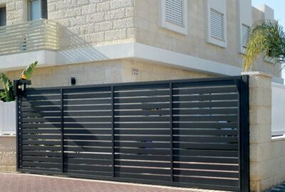 Black horizontal slat sliding gate in front of a modern light-colored stone house.