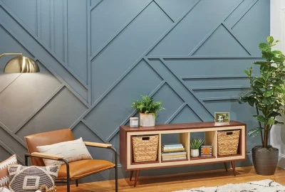 Modern living room with a blue geometric accent wall, leather chair, wood media console, and a large potted plant.
