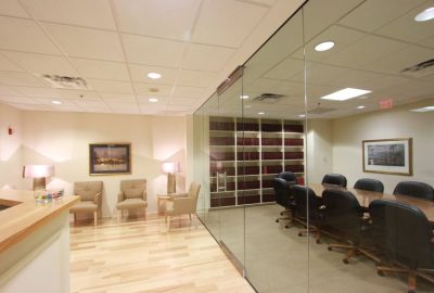 Modern office interior with a waiting area and a glass-walled conference room containing a law library.
