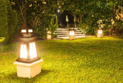 Illuminated Japanese pagoda lanterns on a grassy lawn in a lush garden at night.