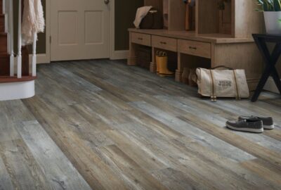 Wide-plank rustic wood-look flooring in an entryway with a mudroom bench, shoes, and a bag.