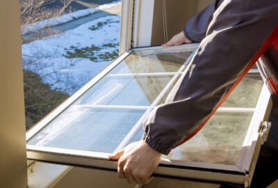 Person removing a cracked window pane from a window frame, with a snowy landscape visible outside.