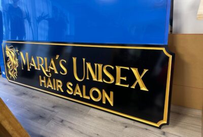 Black and gold sign for Maria's Unisex Hair Salon with a stylized hair logo.
