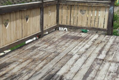 Weathered wooden deck with a railing featuring heart-shaped cutouts.