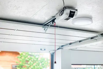 Garage door opener motor mounted to the ceiling with a red emergency release cord hanging down.