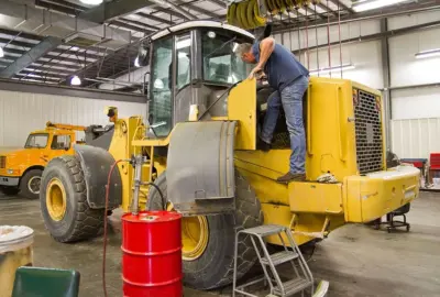Man performing maintenance on a large yellow industrial vehicle inside a service garage.