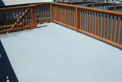 Light gray coated deck surface with wooden railings overlooking a marina.